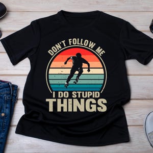 Puede incluir: Camiseta negra con un gráfico de estilo vintage de una persona en patines. El gráfico dice "No me sigas, hago cosas estúpidas".