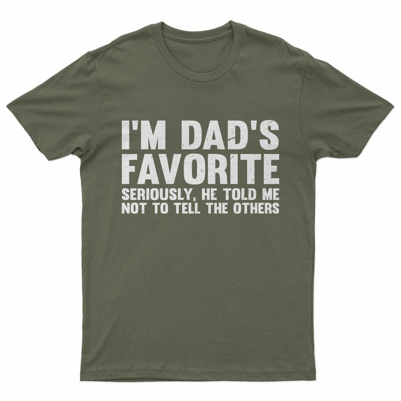 May include: Olive green t-shirt with the text "I'M DAD'S FAVORITE" in large white letters. Below, smaller text reads "SERIOUSLY, HE TOLD ME NOT TO TELL THE OTHERS". A casual, humorous tee.