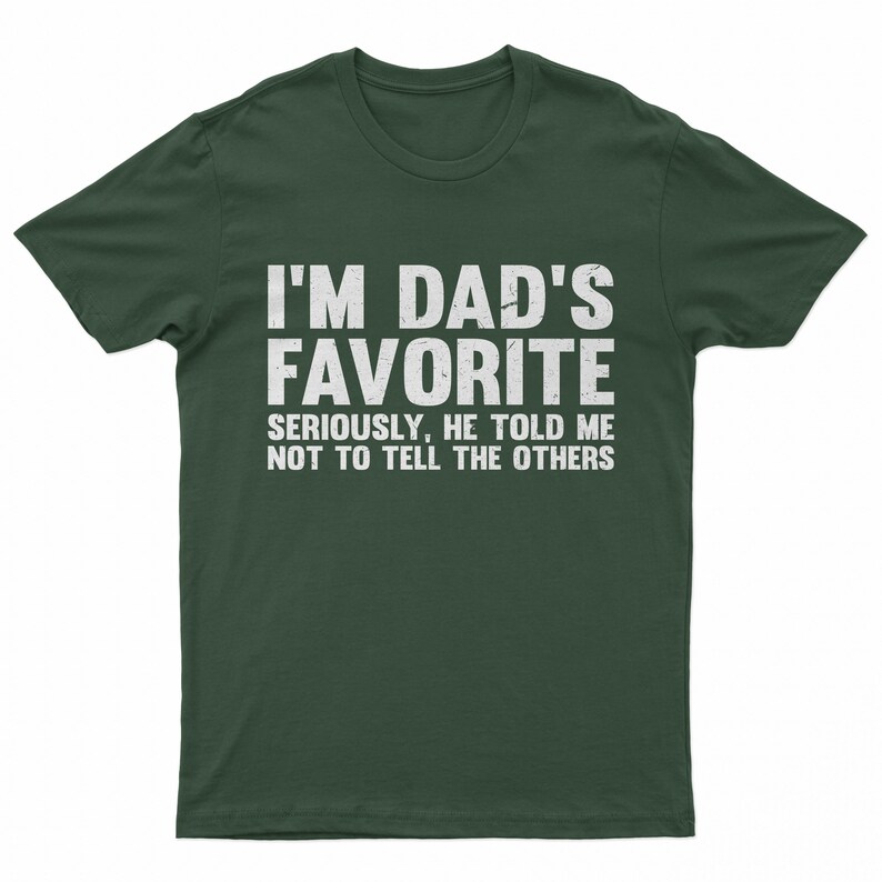 May include: Dark green t-shirt with the text "I'M DAD'S FAVORITE" in large white letters. Below, smaller text reads "SERIOUSLY, HE TOLD ME NOT TO TELL THE OTHERS". A humorous graphic tee.