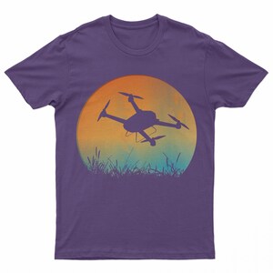 May include: Purple t-shirt with a silhouette of a drone flying in front of a sunset.
