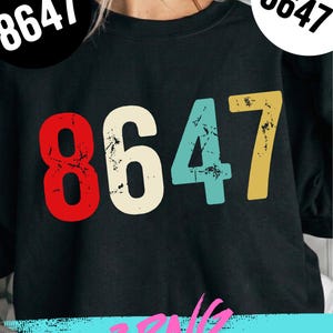 Peut inclure: Sweat-shirt noir avec le nombre "8647" en rouge, blanc cassé, bleu sarcelle et jaune. Les chiffres ont un aspect vieilli. Le texte "8647" est également imprimé dans un cercle blanc en haut à gauche et à droite.