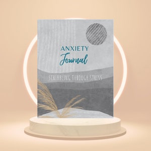 Może przedstawiać: Dziennik lęków z szarą i białą okładką, z napisem "ANXIETY Journal" w turkusowym skrypcie i "SCRIBBLING THROUGH STRESS" w kolorze szarym. Projekt okładki zawiera teksturowane koło i abstrakcyjny krajobraz.