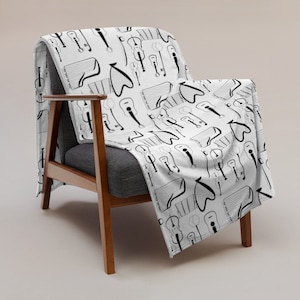 May include: A white throw blanket with a black and white musical instrument pattern. The blanket is draped over a wooden armchair with a gray cushion.