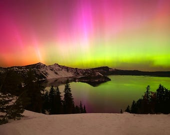 May include: A vibrant aurora borealis display in shades of pink, green, and yellow over a dark mountain range and a still lake. The sky is filled with colorful light, creating a stunning natural spectacle.