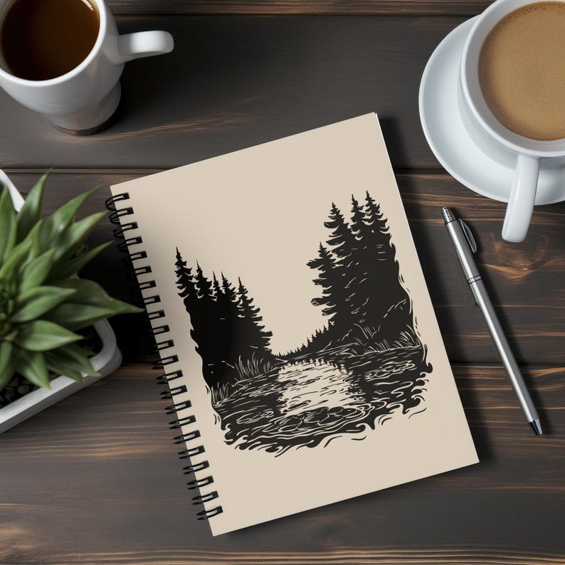 May include: Spiral-bound notebook featuring a black and white illustration of a forest scene with a river. The notebook has a cream-colored cover and a black spiral binding. A pen and two cups of coffee are also visible.