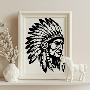 May include: Black and white framed print of a Native American chief in profile, wearing a feathered headdress. The artwork is displayed on a white shelf, accompanied by a white vase with dried flowers and a white horse figurine.
