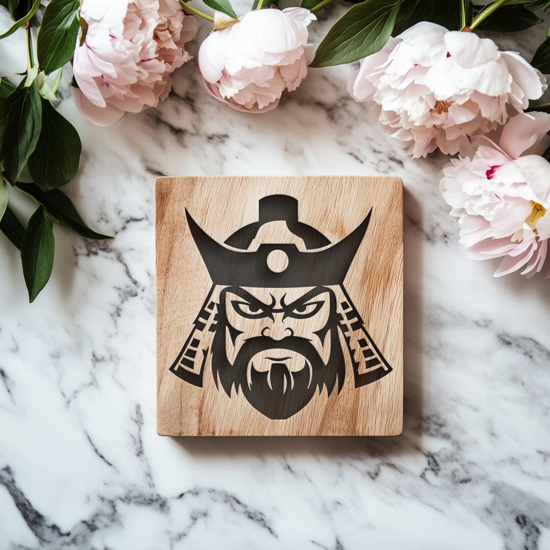 K&ouml;nnte beinhalten: Ein quadratischer Holzuntersetzer mit einem schwarzen Samurai-Krieger-Design. Der Untersetzer besteht aus hellfarbenem Holz und zeigt eine detaillierte Illustration des Gesichts eines Samurai. Rosa Pfingstrosen und gr&uuml;ne Bl&auml;tter befinden sich im Hintergrund.