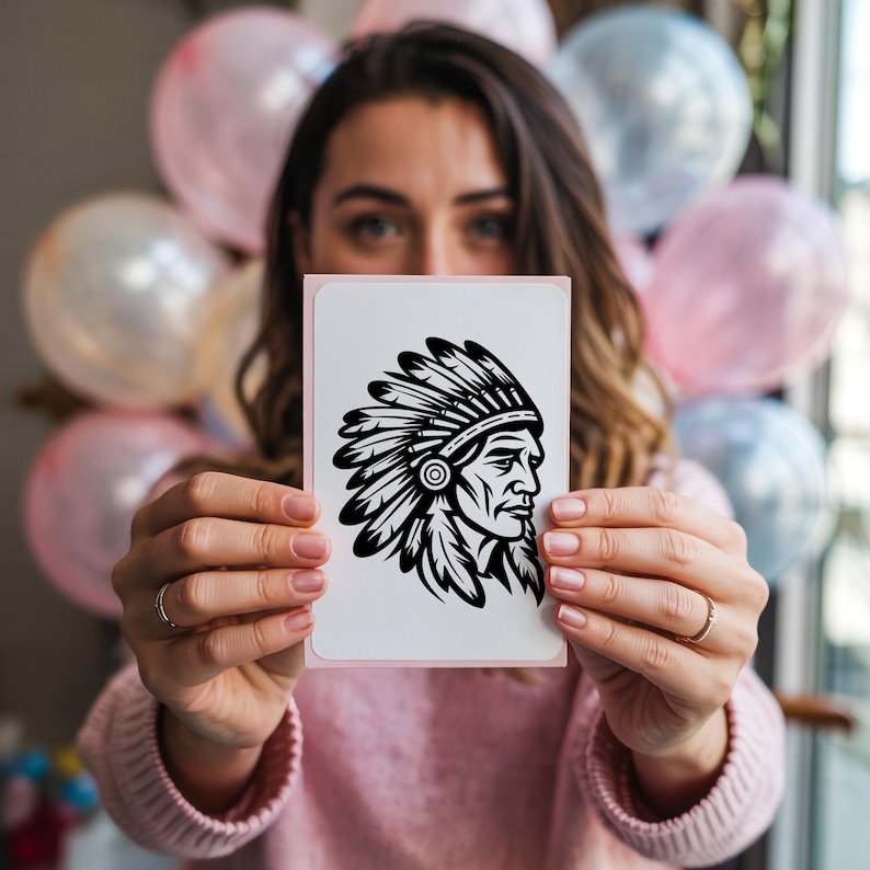May include: A white card with a pink border featuring a black and white illustration of a Native American chief in profile. The chief is wearing a feathered headdress. The card is held in front of a person, with balloons in the background.