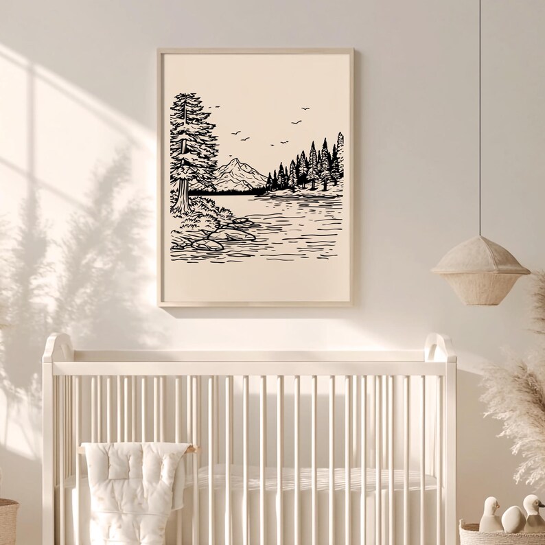 May include: Black and white landscape art print featuring a mountain, lake, and trees. The artwork is framed in a light wood frame and hangs above a white crib. The art print has a minimalist style.