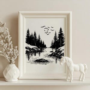 May include: Black and white framed art print depicting a serene forest scene with a river, trees, and birds in flight. A white ceramic horse figurine and a white vase with dried flowers are on a shelf in front of the print.