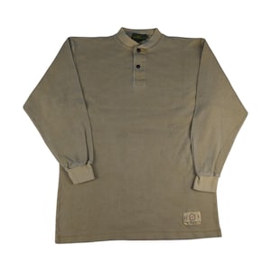 Könnte beinhalten: Ein langärmeliges, hellbraunes Hemd mit Knopfkrag und einer einreihigen Knopfleiste. Das Hemd hat einen kleinen, rechteckigen Aufnäher unten rechts mit dem aufgedruckten Text "U.S. Navy".