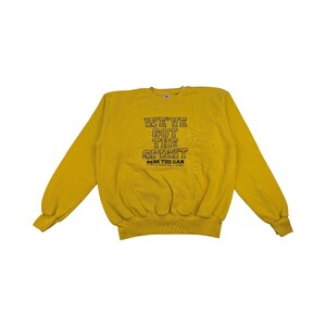 May include: Mustard yellow sweatshirt with long sleeves. The front features the text "WE'VE GOT THE SPIRIT" in a distressed font. Below the text is "HERE YOU CAN" and the name of a basketball school.