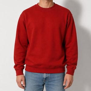 Könnte beinhalten: Ein einfarbiges rotes Sweatshirt mit Rundhalsausschnitt und langen Ärmeln. Das Sweatshirt wird mit einer blauen Jeans getragen. Der Stil ist lässig und bequem. Das Material scheint weich zu sein.