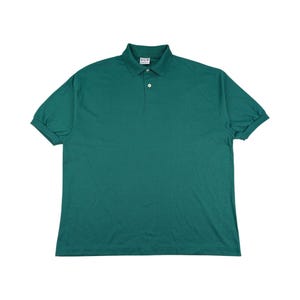 Könnte beinhalten: Ein einfarbiges, teal-farbenes Poloshirt mit kurzen Ärmeln. Das Shirt hat einen klassischen Kragen, eine Knopfleiste mit drei Knöpfen und eine lockere Passform. Der Stoff scheint ein leichter Strick zu sein, der sich für Freizeitkleidung eignet. Das Shirt wird vor weißem Hintergrund gezeigt.