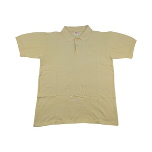 Op de afbeelding: Een lichtgeel poloshirt met korte mouwen, een kraag en een knoopsluiting met drie knopen. Het shirt heeft een klein logo op de borst en is gemaakt van een zachte, ademende stof.