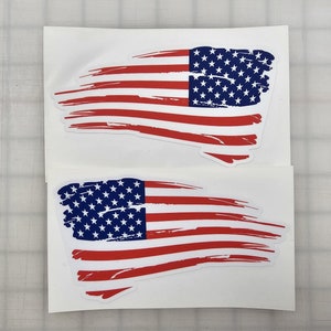 May include: Two white sheets of paper with a distressed American flag design printed on each. The flags are red, white, and blue with a white background.