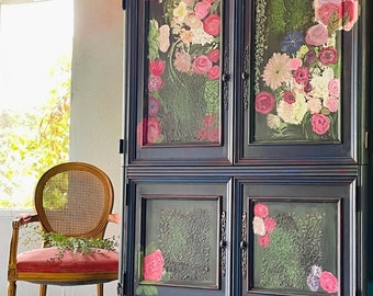 Può includere: Un armadio in legno scuro con intagli decorativi e motivi floreali dipinti sulle porte. L'armadio ha due ante superiori e due ante inferiori, tutte con pannelli di vetro. L'armadio è posizionato su un pavimento grigio chiaro.