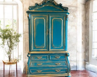 Può includere: Un armadio alto e decorato con una finitura blu turchese e dettagli dorati. L'armadio ha due ante con modanature decorative e quattro cassetti sotto. L'armadio è in piedi su un pavimento di legno.
