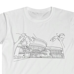 以下が含まれることがあります： 白いTシャツに、黒い線で描かれたヤシの木の前にある建物の絵が描かれています。建物には「カジノ」と書かれています。