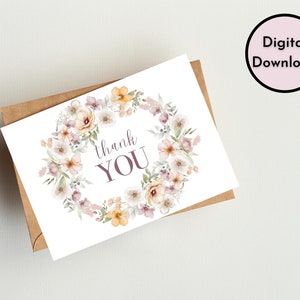 May include: A white card with a floral wreath design in shades of pink, yellow, and green. The text "thank you" is written in purple inside the wreath.