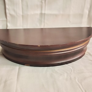 May include: A semi-circular, dark brown wooden shelf with a curved front edge. The shelf has a layered design with a slightly distressed finish, showing some wear and tear. The shelf is designed to be mounted on a wall.