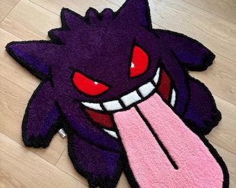 Puede incluir: Una alfombra tufting con la forma del personaje Gengar, que presenta un cuerpo de color morado oscuro, ojos rojos brillantes, una amplia sonrisa con dientes blancos y una larga lengua rosa claro, todo con un borde negro grueso.