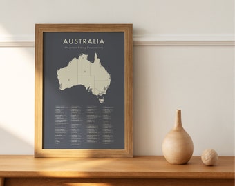 May include: A framed print of a map of Australia with the title "Australia Mountain Biking Destinations". The map is in beige and white on a dark grey background. The print is in a light brown wooden frame and is sitting on a light brown wooden table.