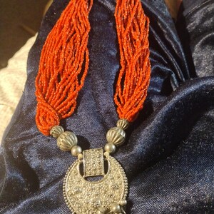 May include: A silver pendant necklace with a large, round, ornate charm and a long strand of red beads.