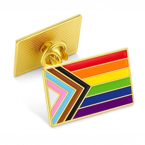 May include: Two gold-colored enamel pins. One is rectangular, the other is a flag-shaped pin with a rainbow design and a black, brown, pink, blue, and white chevron. The pins have a gold-colored pin back.