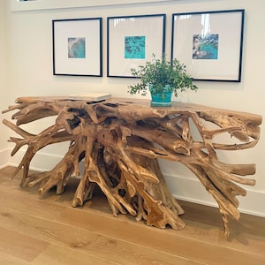 May include: A natural wood console table with a unique root-like base. Three framed square art prints hang above the table. A small potted plant sits on the table's surface, along with a book. The room has a modern design with a large window.