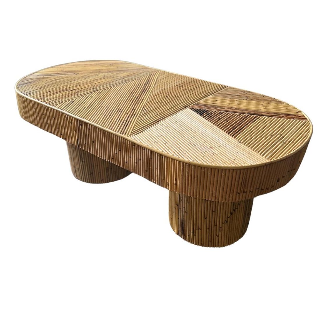 May include: A large oval-shaped coffee table made of woven natural materials. The table has a geometric pattern and is supported by two cylindrical legs.