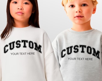 May include: Two children wearing matching sweatshirts. One sweatshirt is white, the other is gray. Both sweatshirts have the word "CUSTOM" in black block letters across the chest, with "YOUR TEXT HERE" below.