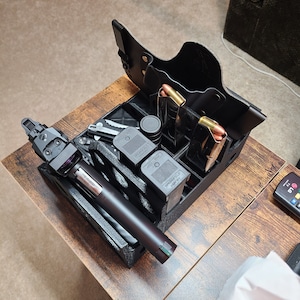 May include: A black gun holster with multiple magazine holders and a black gun with a green laser sight. The holster is made of leather and has a brown stitching detail. The gun is resting in the holster and the magazine holders are filled with magazines.
