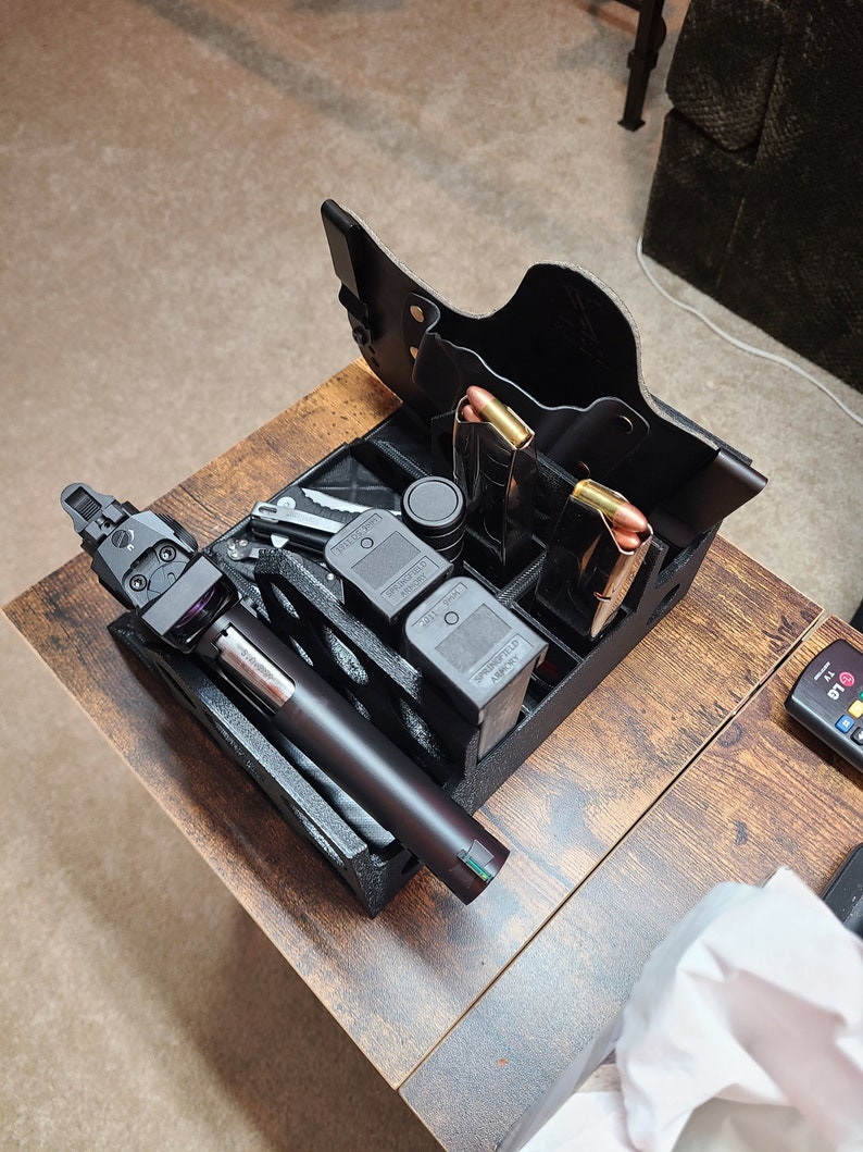 May include: A black gun holster with multiple magazine holders and a black gun with a green laser sight. The holster is made of leather and has a brown stitching detail. The gun is resting in the holster and the magazine holders are filled with magazines.