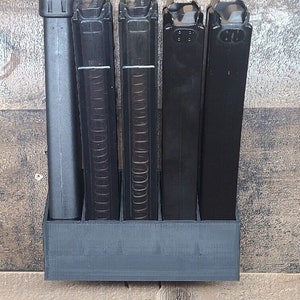 May include: A black plastic magazine holder with four slots for magazines and a single slot for a cleaning rod. The holder is mounted on a wooden wall.