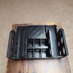 May include: Black 3D printed organizer with multiple compartments and slots. The organizer has a grid of small squares and a row of round holes on each side.