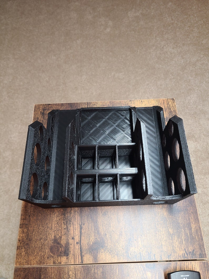 May include: Black 3D printed organizer with multiple compartments and slots. The organizer has a grid of small squares and a row of round holes on each side.
