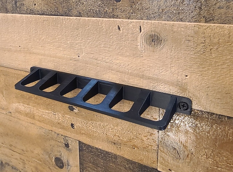 May include: Black plastic wall-mounted organizer with six slots. The organizer is mounted on a wood wall.