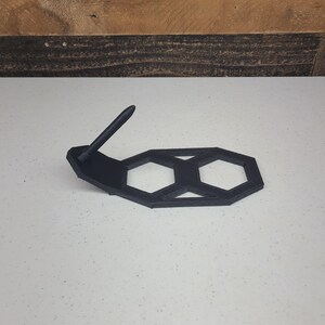 K&ouml;nnte beinhalten: Ein schwarzer, 3D-gedruckter sechseckiger St&auml;nder mit einem Stifthalter. Der St&auml;nder ist aus Kunststoff und hat ein geometrisches Design.