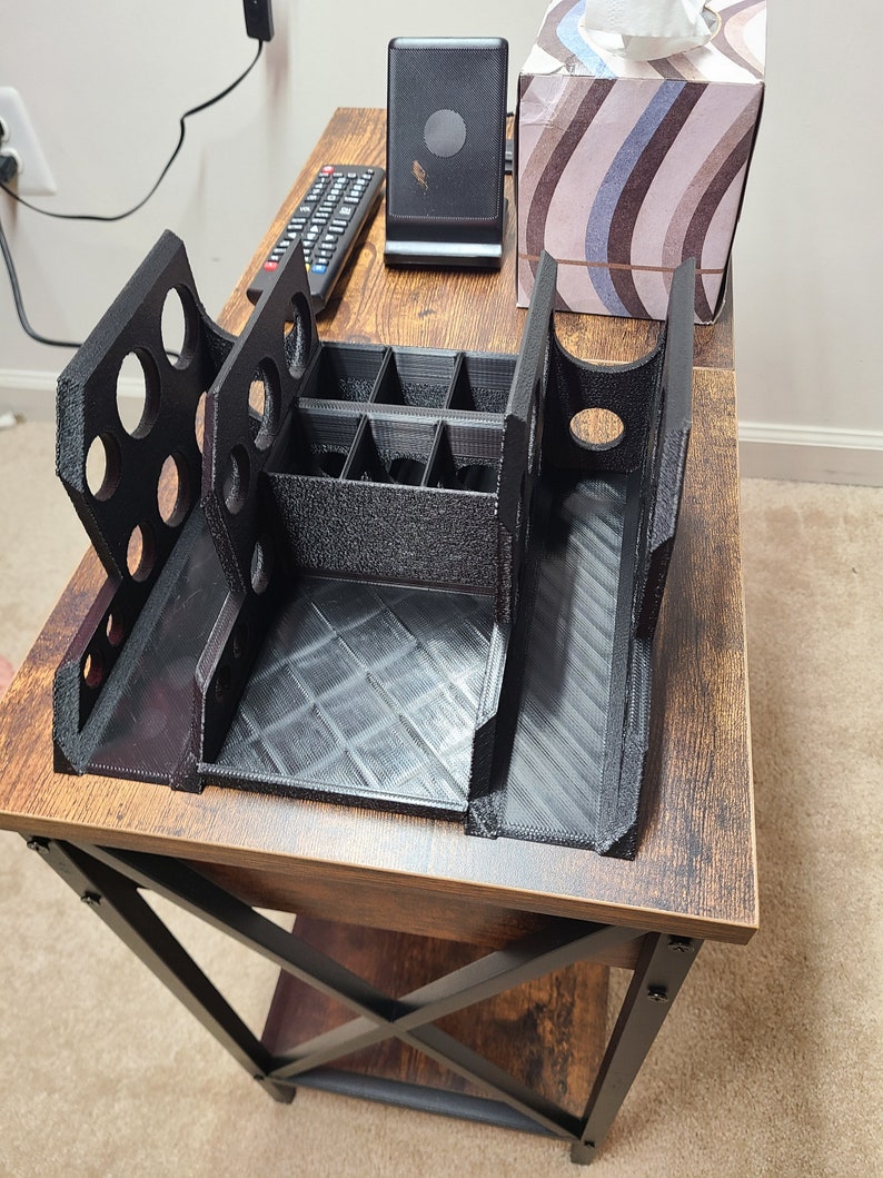 May include: A black plastic organizer with multiple compartments and slots. The organizer is sitting on a wooden table with a black metal frame.