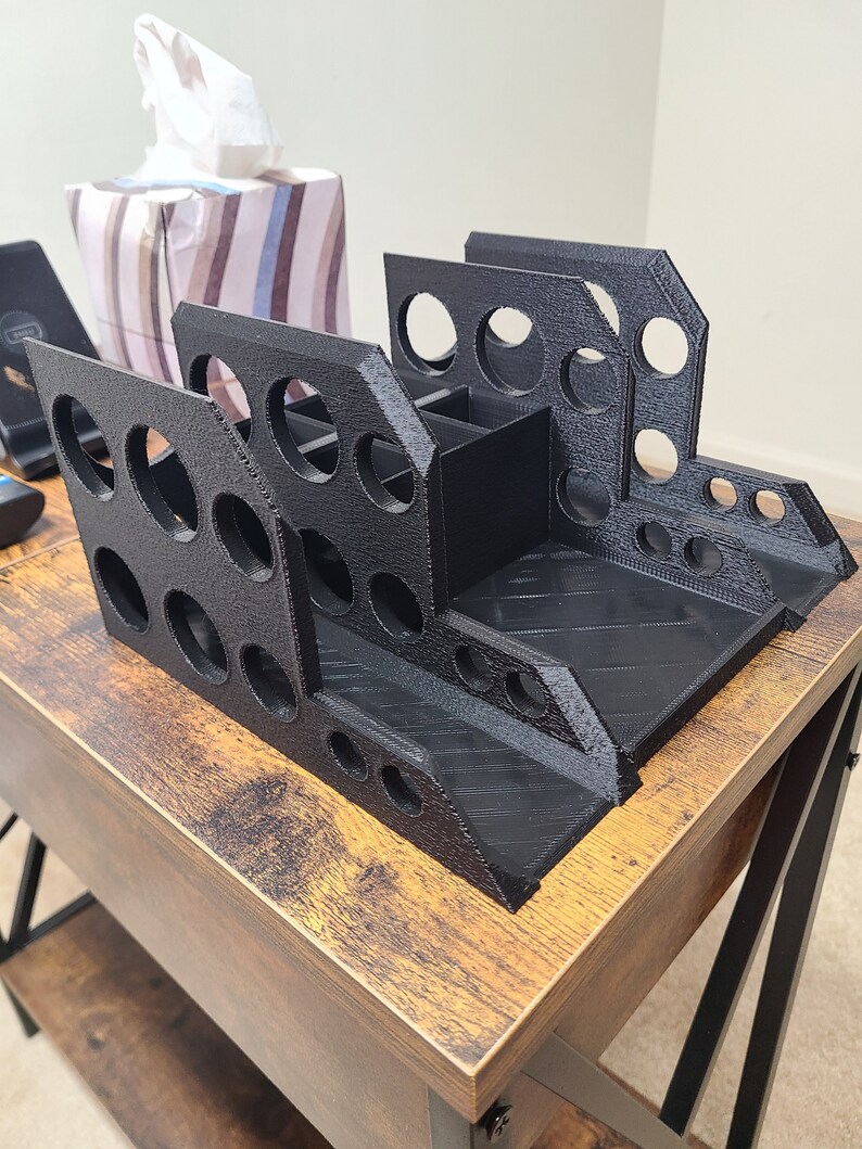 May include: A black plastic desk organizer with multiple compartments and holes for pens, pencils, and other office supplies. The organizer is sitting on a wooden table.