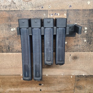 May include: Four black magazine holders mounted on a wooden wall. The holders are made of plastic and have a textured surface.