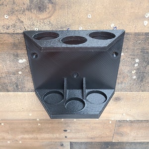 May include: A black, wall-mounted organizer with three circular openings on top and three on the bottom. The organizer is made of a textured material and is mounted on a wooden surface. The design is geometric and functional.