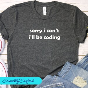 Puede incluir: Una camiseta gris oscuro con el texto "sorry i can't i'll be coding" en letras blancas.