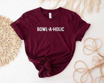 Może przedstawiać: Bordowy t-shirt z nadrukiem "BOWL-A-HOLIC" w kolorze białym na przodzie.