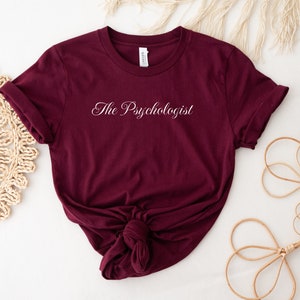 Könnte beinhalten: Burgunderfarbenes T-Shirt mit weißem Text, der "The Psychologist" lautet.
