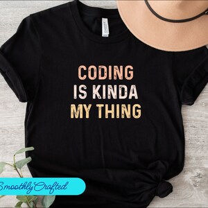 Puede incluir: Camiseta negra con el texto "Coding is kinda my thing" en un esquema de colores melocotón y amarillo.
