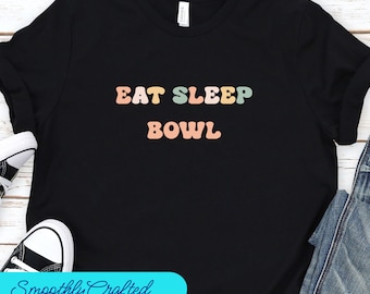 May include: Black t-shirt with the text "Eat Sleep Bowl" in colorful, retro-style lettering.
