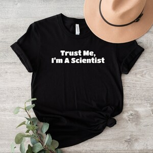 Pode incluir: Camiseta preta com texto branco que diz "Trust Me, I'm A Scientist".