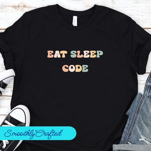 Pode incluir: Camiseta preta com o texto "Eat Sleep Code" em letras retrô coloridas.